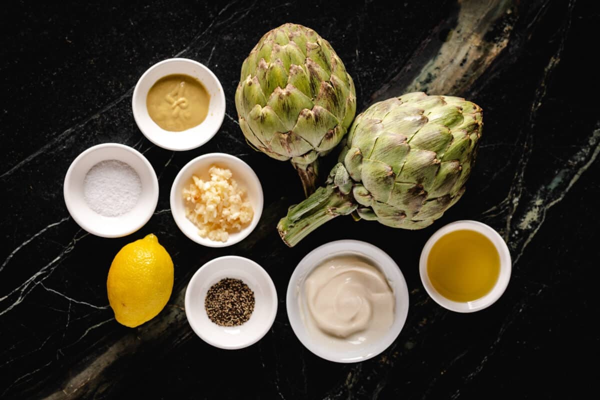 An overhead shot of artichoke halves, and bowls of ingredients for a dressing.