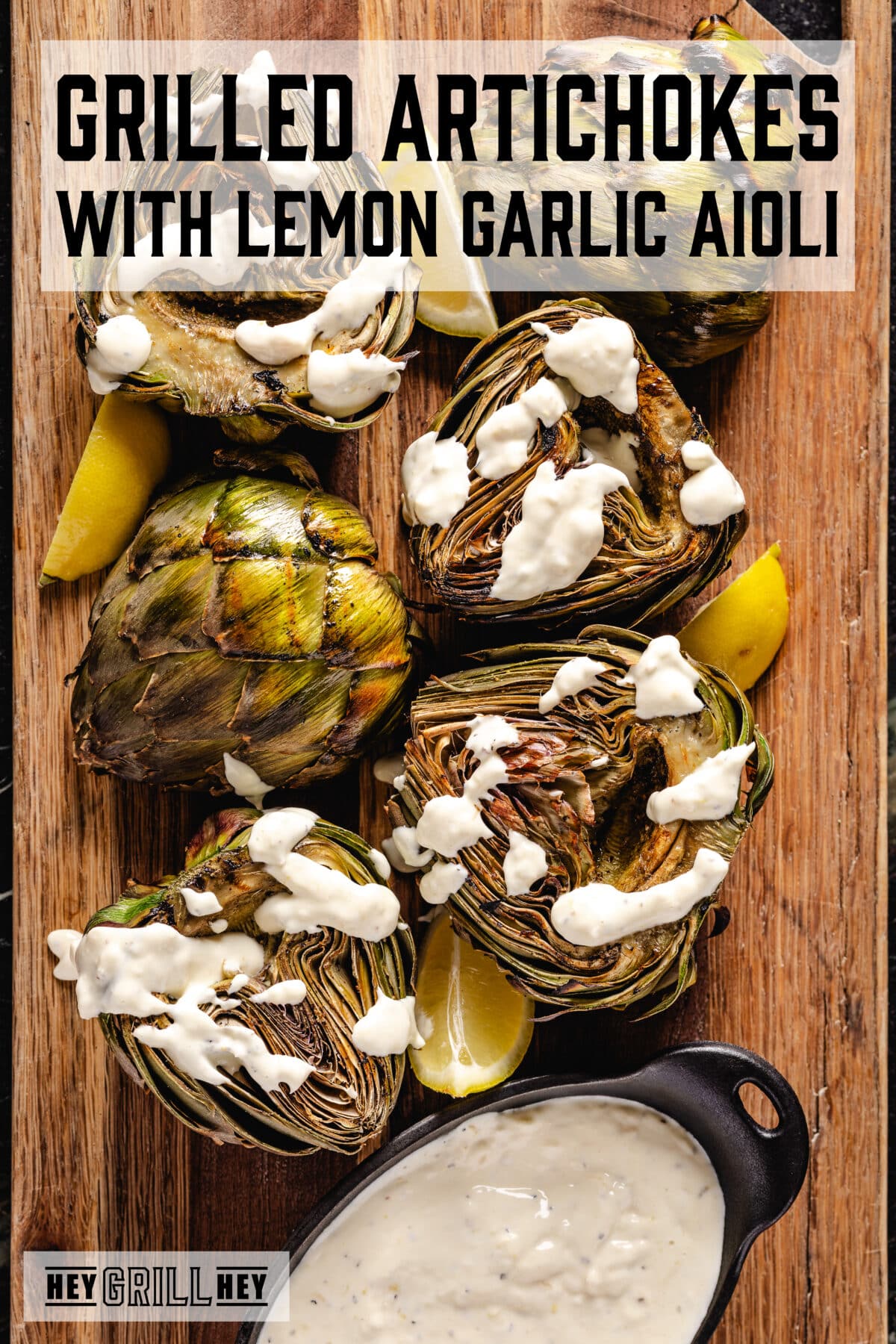 An overhead shot of grilled artichoke halves on a wooden cutting board. The text overlay reads "Grilled Artichokes with Lemon Garlic Aioli" at the top, and "Hey Grill Hey" at the bottom.