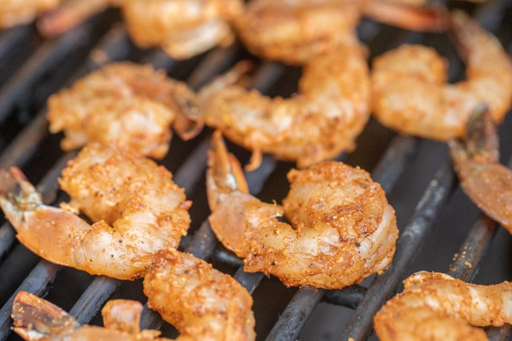 Seasoned shrimp on the grill grates of a charcoal grill.