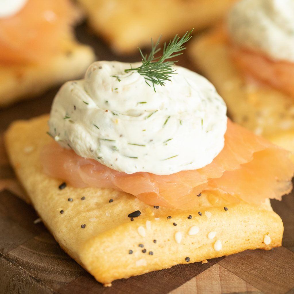 Crescent dough crostini topped with smoked salmon and lemon dill cream cheese on a wooden cutting board.