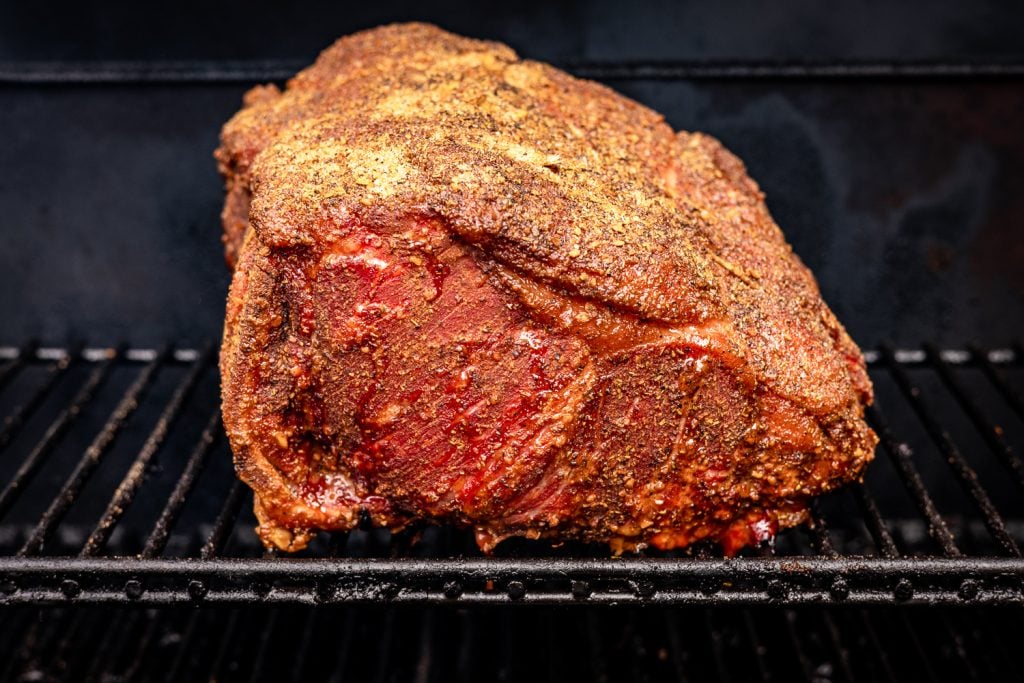 Seasoned New York strip roast on the grill grates of a smoker.
