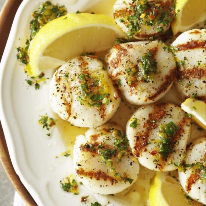 grilled scallops on a white serving plate with lemon wedges.