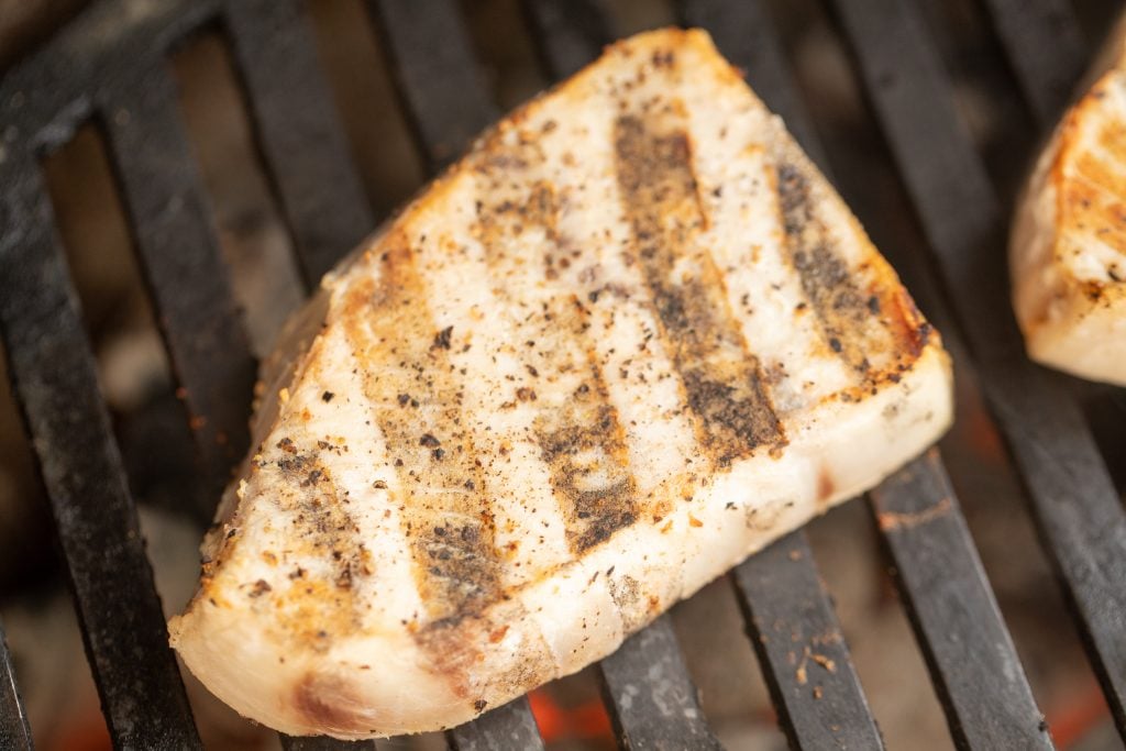 seasoned swordfish on the grill with hot charcoal under the grates.