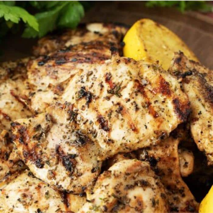 grilled chicken thighs on a wooden serving platter next to lemon wedges and fresh herbs
