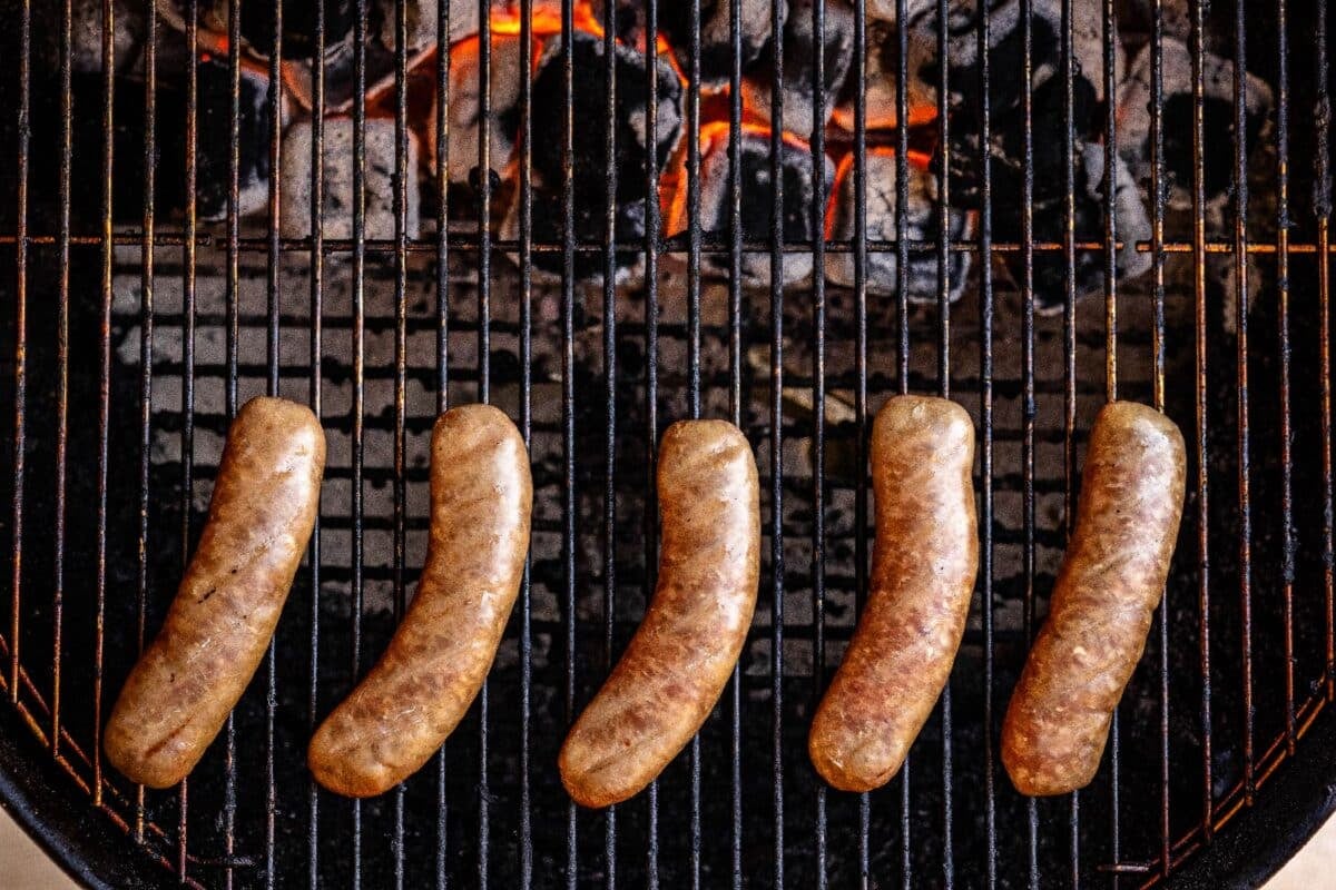 Bratwursts on grill grates over charcoal.