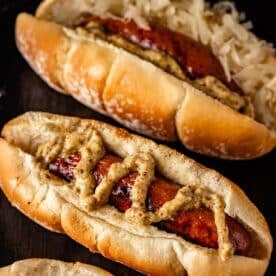 A grilled bratwurst on a rolled drizzled with spicy mustard, and another topped with sauerkraut.