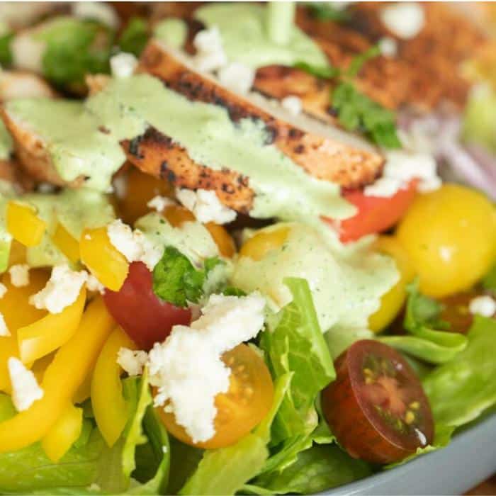 Chopped lettuce topped with sliced tomatoes, yellow bell peppers, sliced chicken breast, and dressing