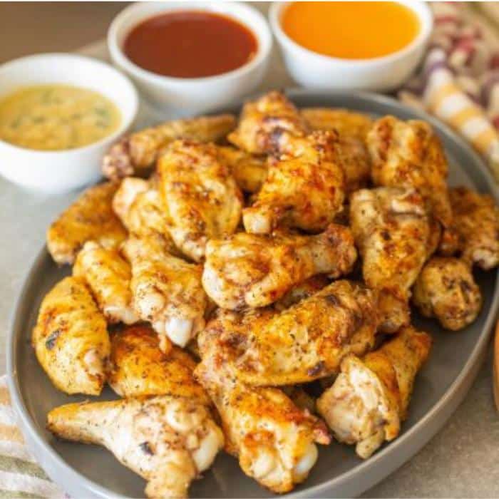 grilled chicken wings on a platter next to three dipping sauces in white bowls