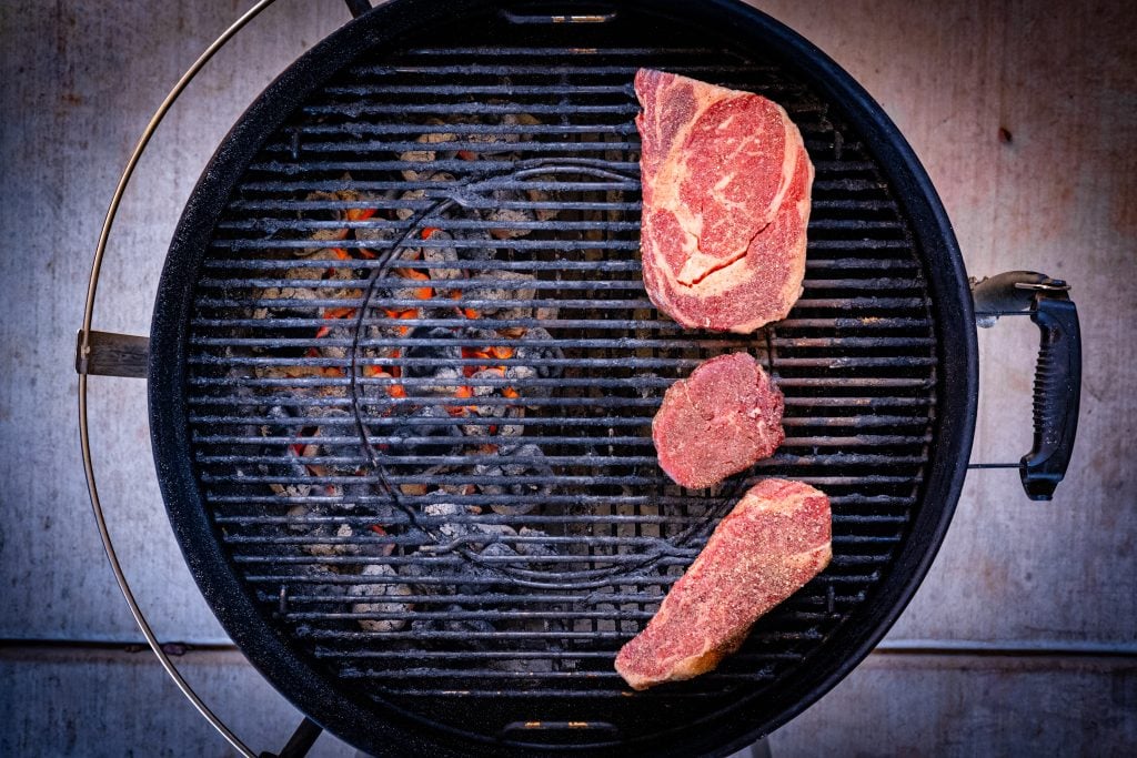 Three steaks over indirect heat on a charcoal grill.