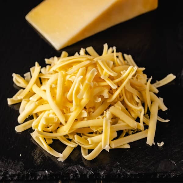 A piled of shredded cheese on a black surface in front of a wedge of cheese.