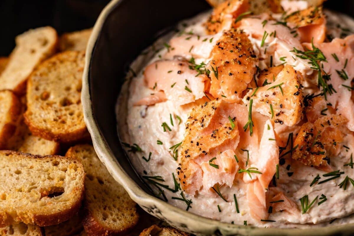 A bowl full of smoked salmon and cream cheese next to toasted slices.