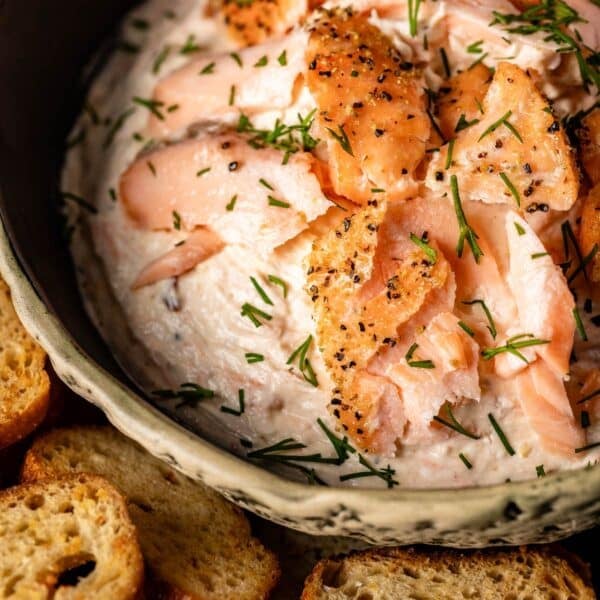 A bowl filled with dip sitting next to crusty bread slices.