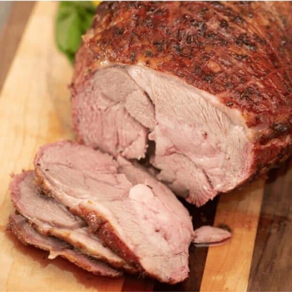 Smoked leg of lamb on a wooden cutting board with three slices laying in front of the roast.