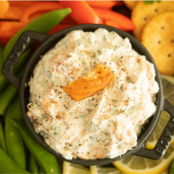 Overhead shot of smoked trout dip in a black bowl surrounded by crackers and sliced veggies.