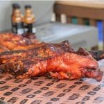 Whole roasted pig on a table covered with butcher paper with two Hey Grill Hey BBQ sauce bottles in the background.