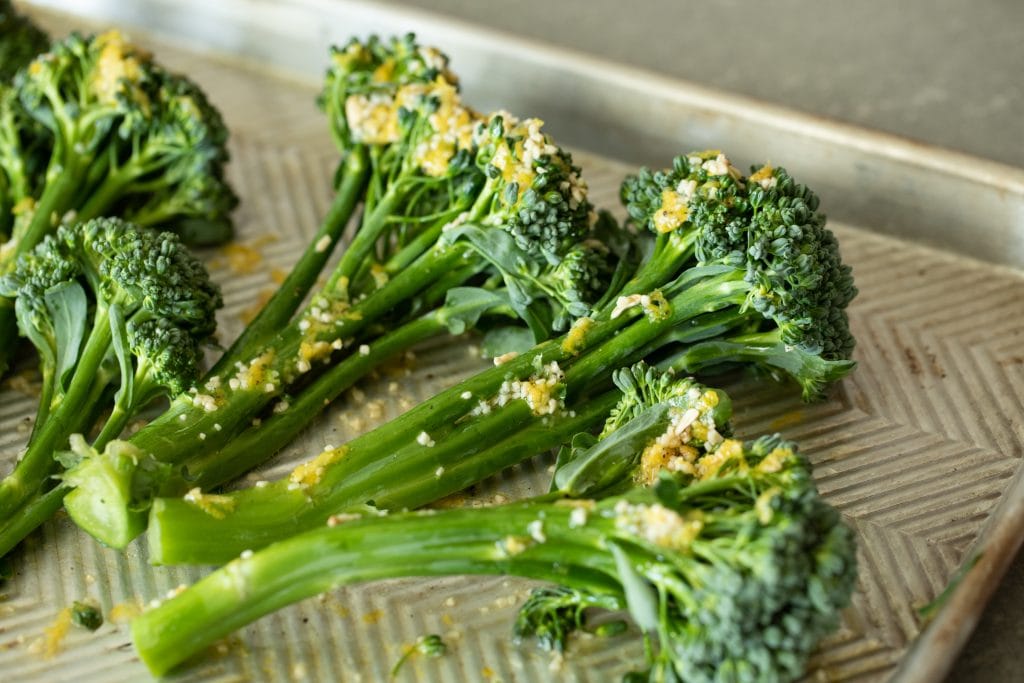 Broccolini drizzled in lemon garlic dressing on a metal baking sheet.
