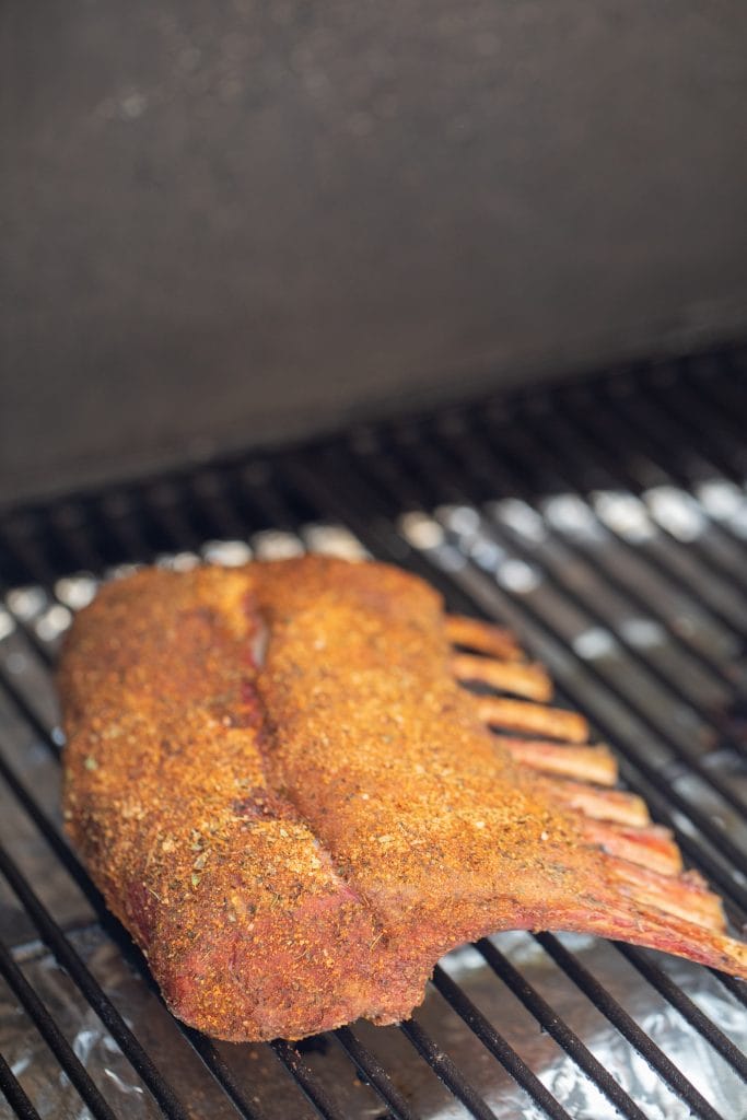 Seasoned rack of lamb in the smoker, about halfway through the cook. The lamb is starting to develop mahogany color from the smoke.