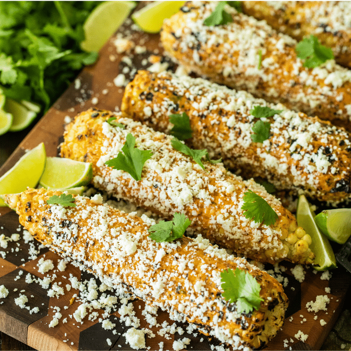 row of Mexican street corn on a wooden cutting board 
