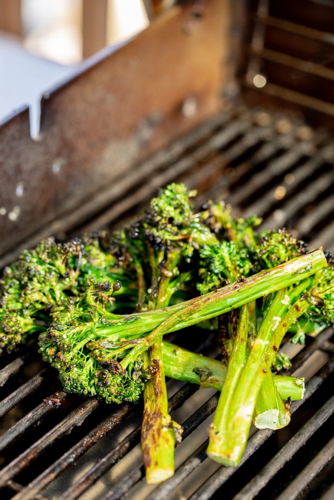 Grilled broccolini piled on the grill grates of a gas grill.