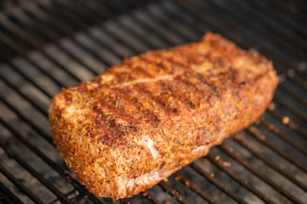 grilled pork loin roast on the grill grates of a charcoal grill.