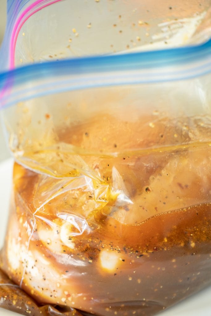 Chicken breasts marinating in brown liquid a gallon-sized zip top bag