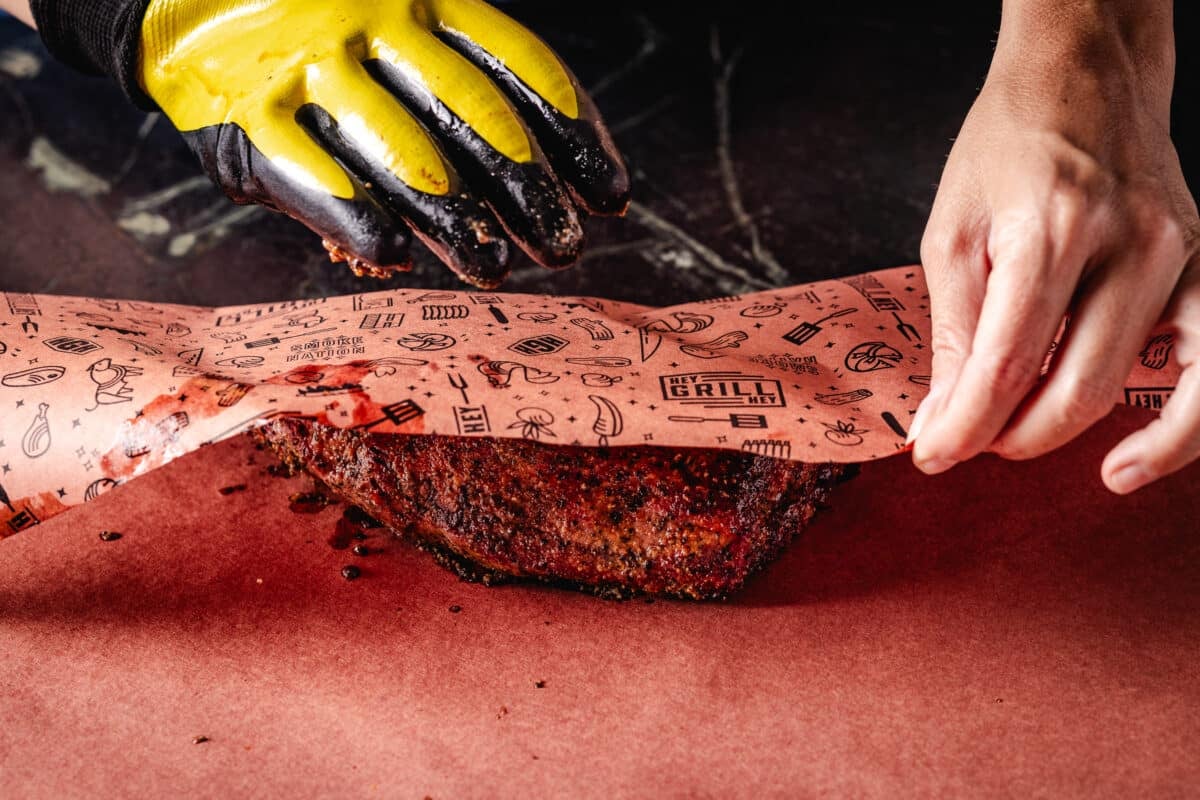 A chef's hands wrapping meat in butcher paper.