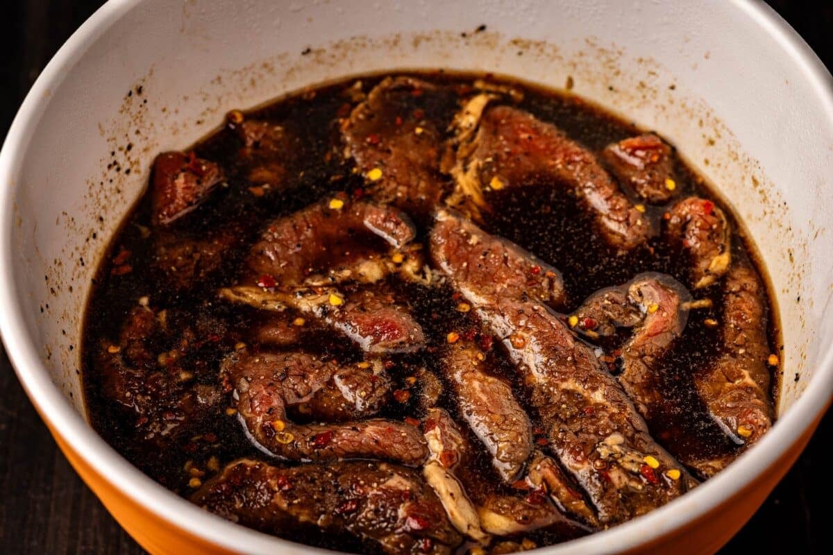 Beef strips marinating in a white bowl.