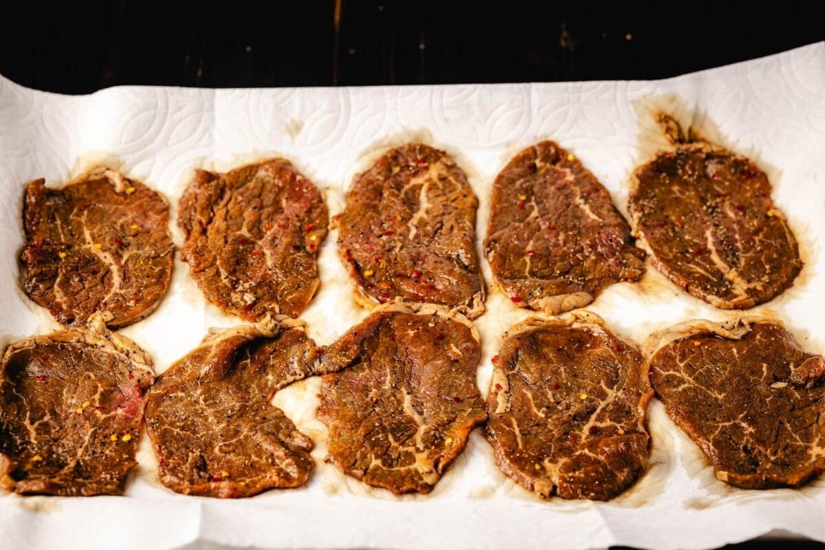 Marinated jerky strips drying on a baking sheet.