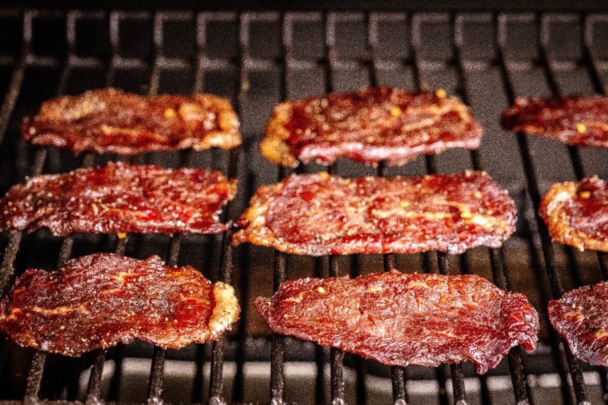 Peppered beef jerky slices drying on smoker grates.