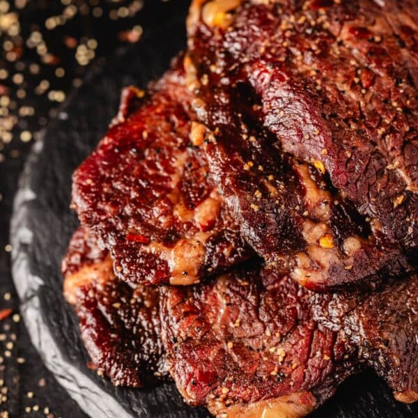 Beef jerky piled on a black plate, and sprinkled with pepper.