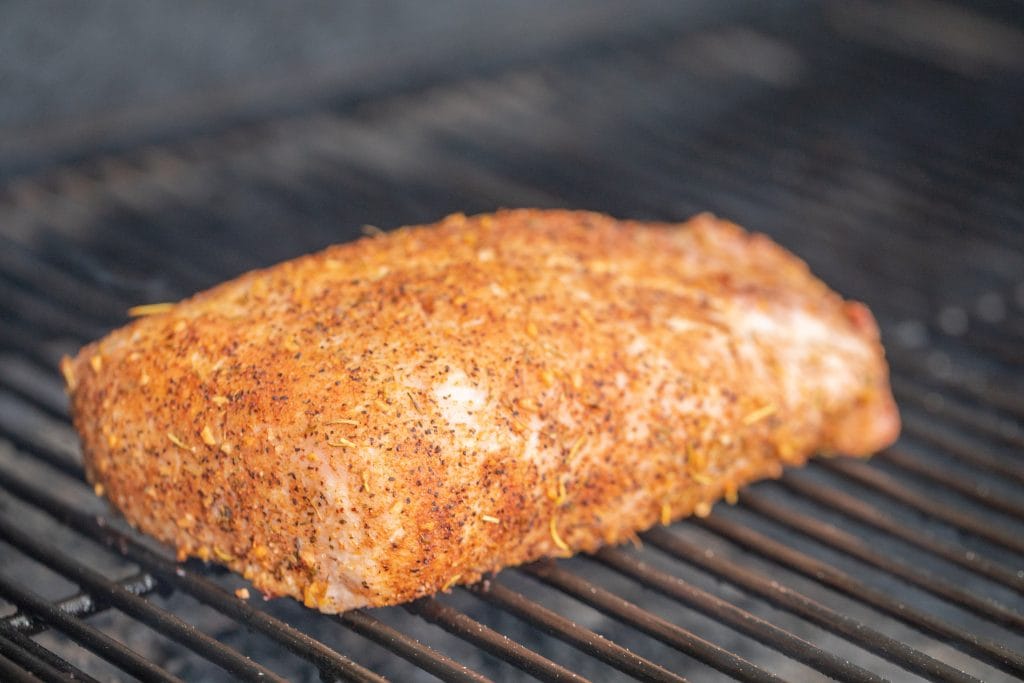whole seasoned pork loin roast on the grill grates of a grill.