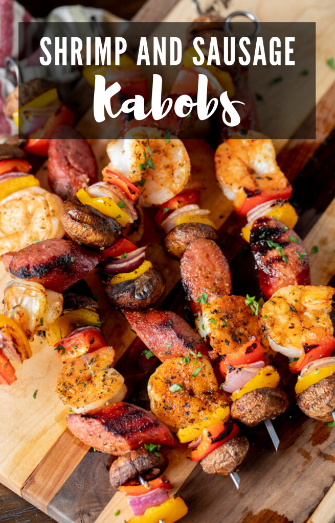 grilled shrimp and sausage kabobs stacked on a wooden cutting board.