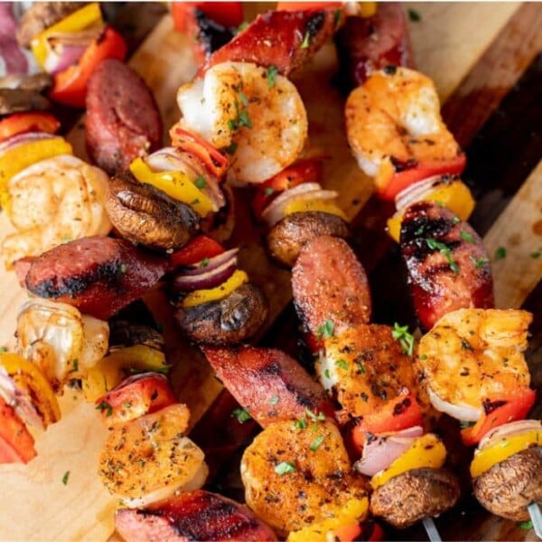 Shrimp and sausage kabobs stacked on a wooden cutting board.
