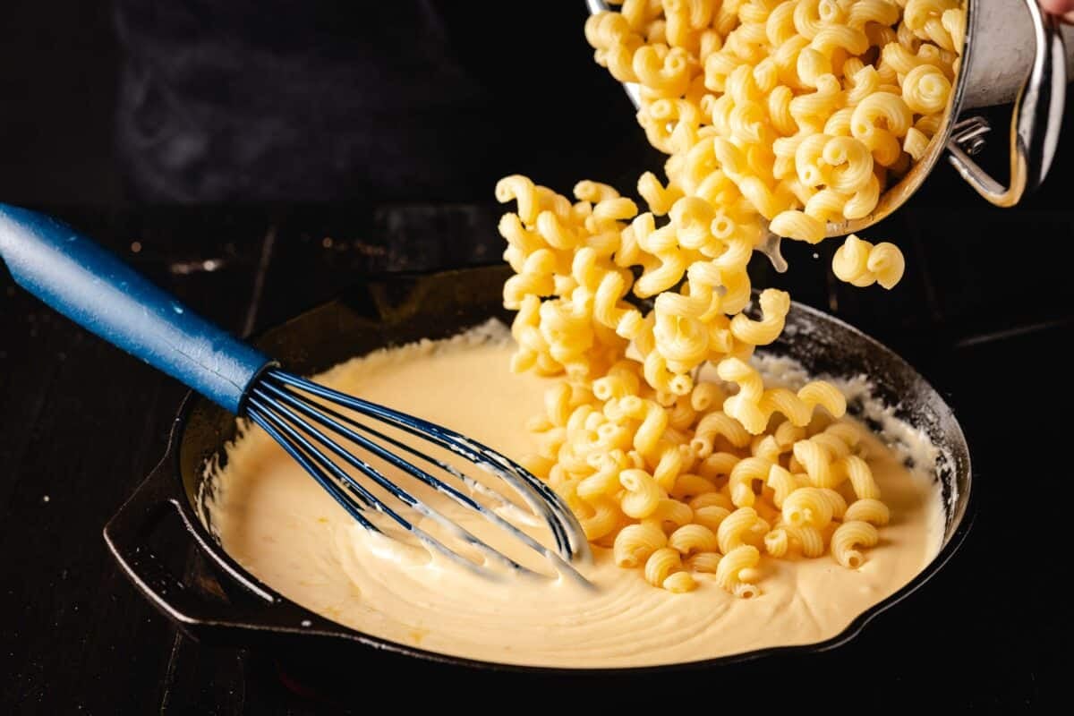 The macaroni are added to a smoked gouda cheese sauce in a pan.