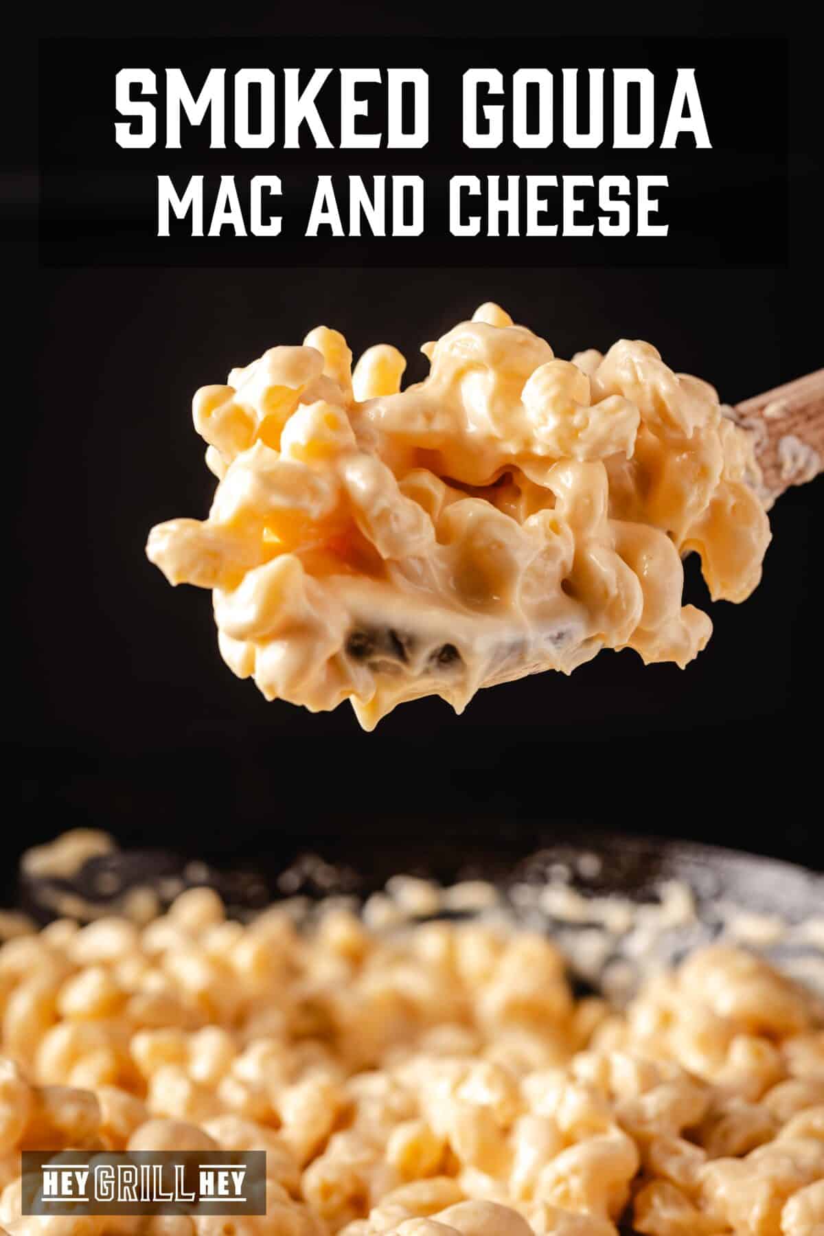 A ball of Mac and cheese on a wooden spoon over a pan. The overlap of the text reads "Gouda Mac and smoked cheese" above, e "Hey Grill Hey" in conclusion.