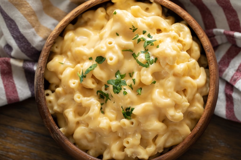 wooden bowl of smoked gouda mac and cheese topped with fresh herbs.