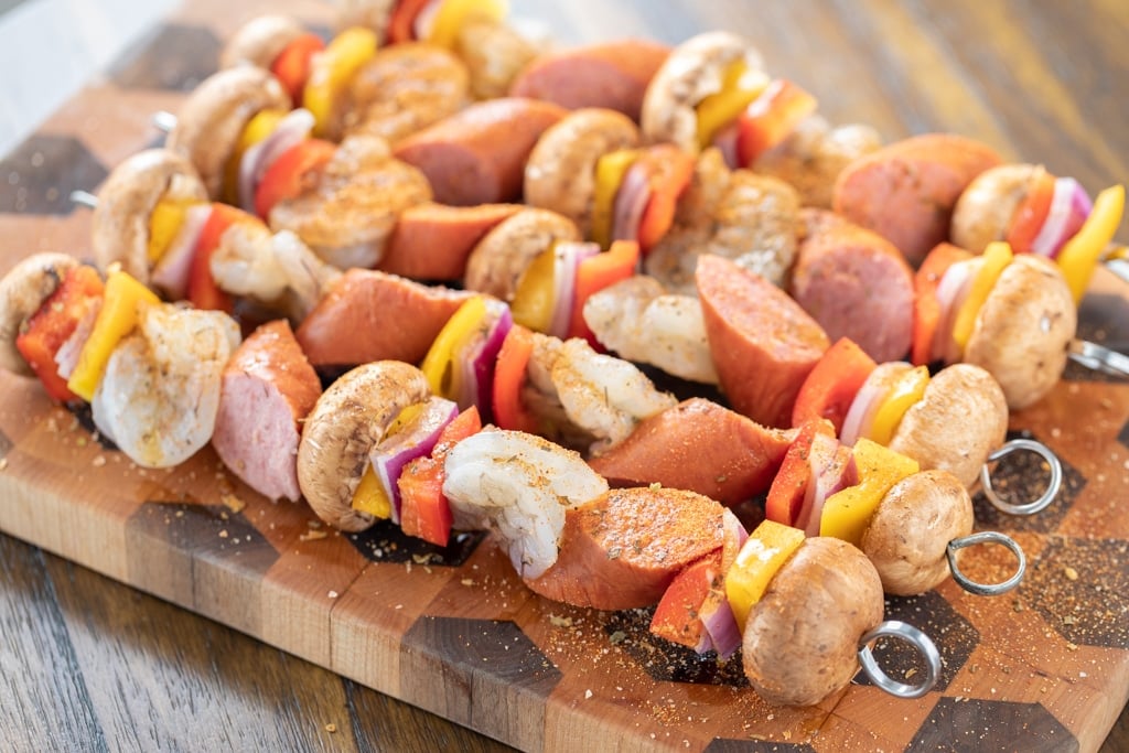 5 assembled shrimp and sausage kabobs on a wooden cutting board.