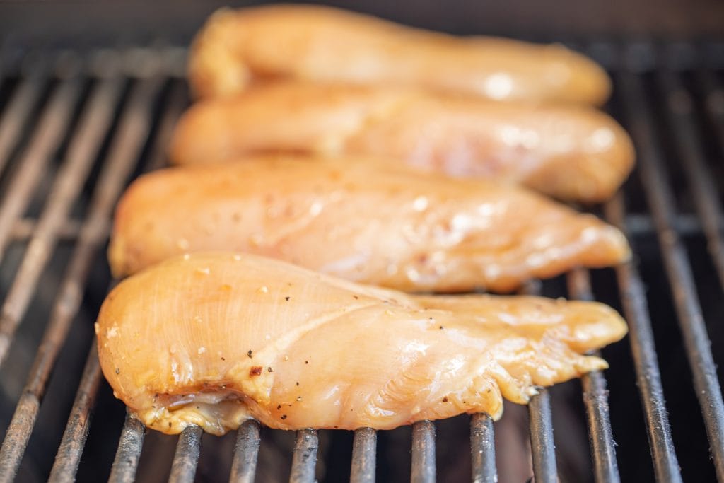 Four marinated chicken breast on the grill grates of a gas grill.