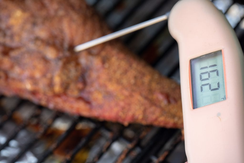 meat thermometer inserted into a tri tip on a grill with the thermometer reading 162 degrees F.