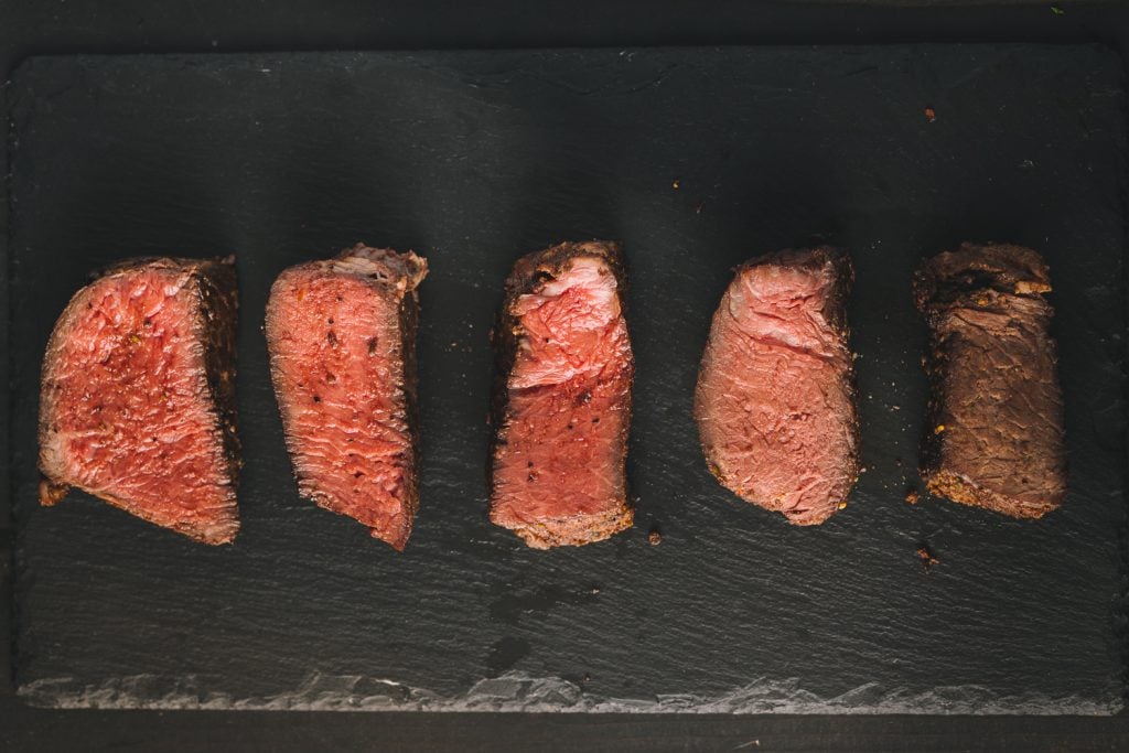 Five steaks on a cutting board ranging from rare to well doneness.