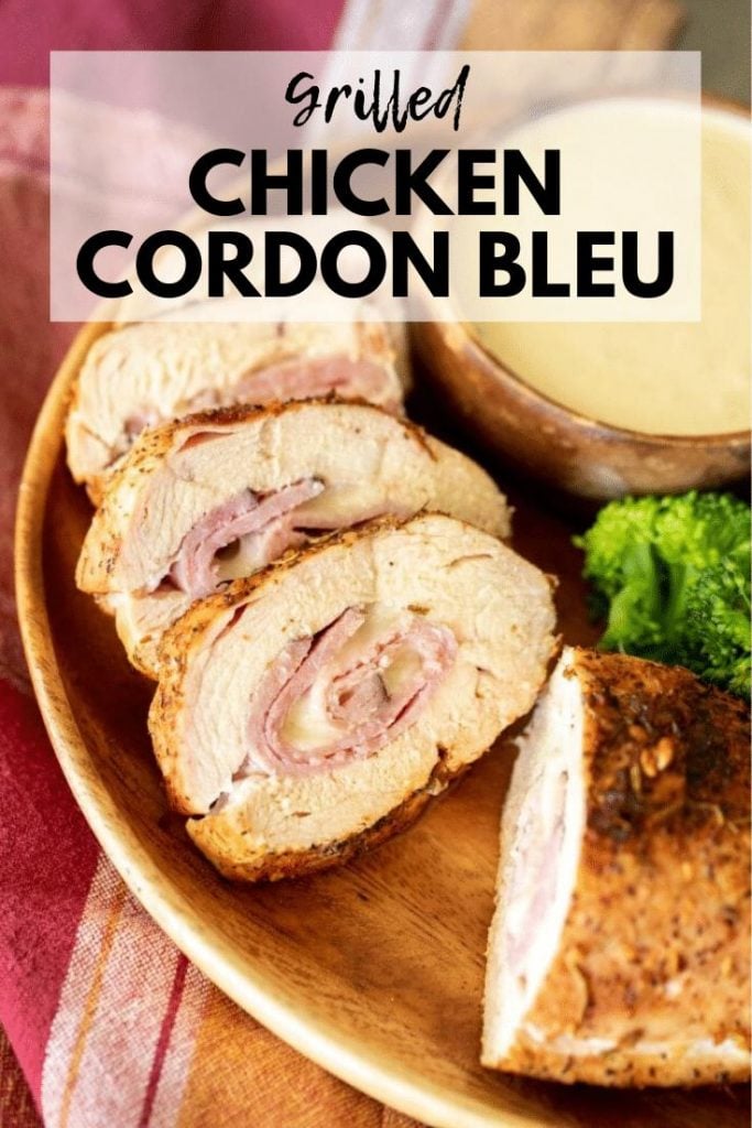 Sliced chicken cordon bleu layered in a wood bowl with a side of broccoli and a bowl of white dipping sauce.