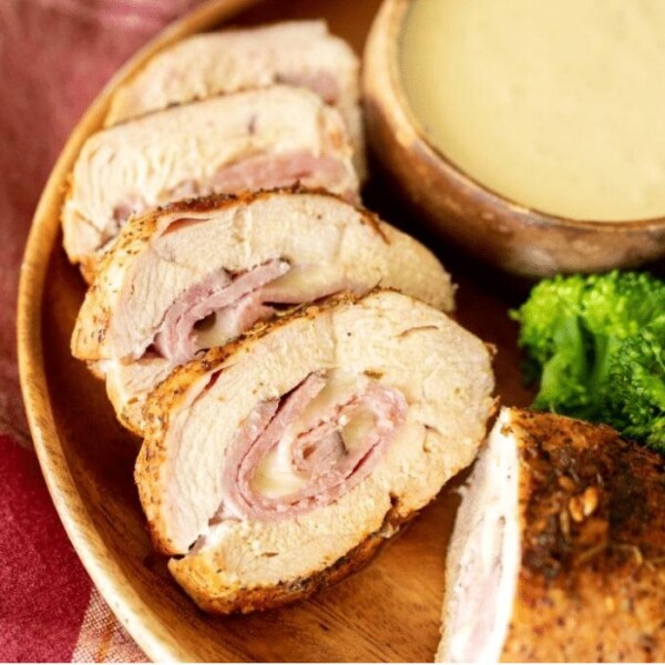 Sliced cross section of grilled chicken cordon bleu next to a bowl of dipping sauce and broccoli florets.
