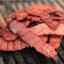Corned Beef Jerky stacked on the grill grates of a smoker.