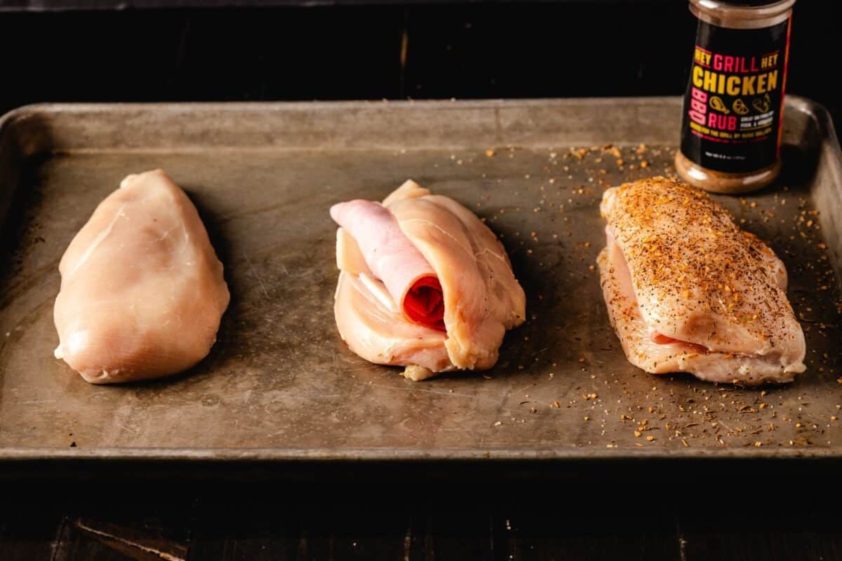 Raw, stuffed chicken breasts on baking sheet.