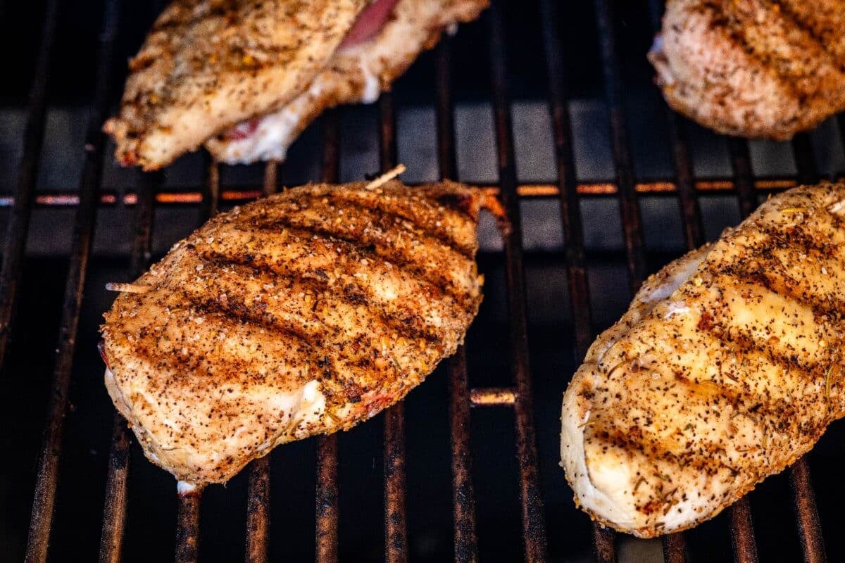 Stuffed chicken breasts on smoker grates with grill marks on top.