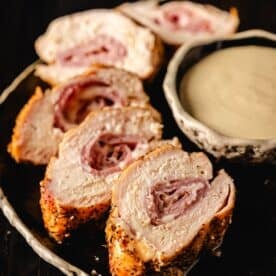 Sliced cross section of grilled chicken cordon bleu next to a bowl of dipping sauce.