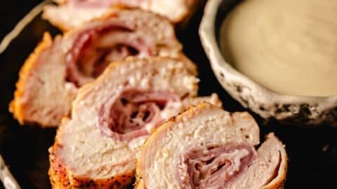 Sliced cross section of grilled chicken cordon bleu next to a bowl of dipping sauce.