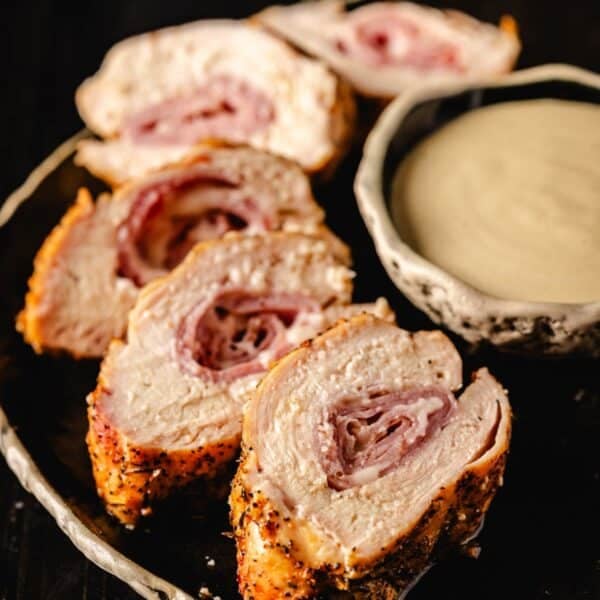 Sliced cross section of grilled chicken cordon bleu next to a bowl of dipping sauce.