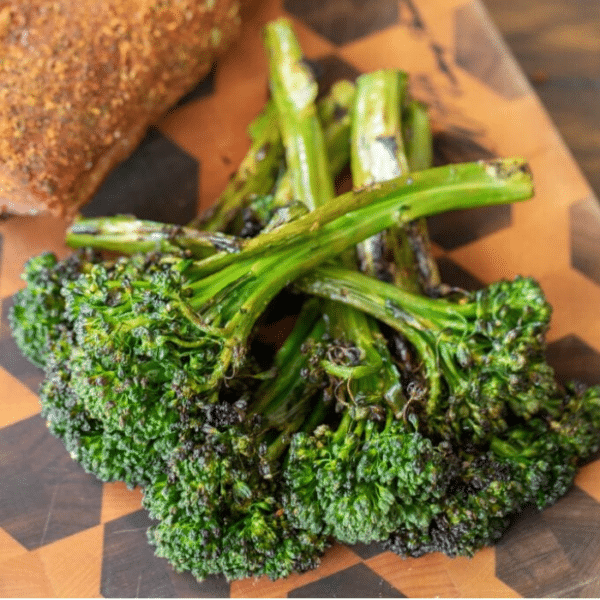Stalks of Grilled broccolini stacked on a wooden cutting board.