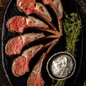 An overhead shot of smoked and sliced lamb with a bowl of seasoned butter and herb garnish.